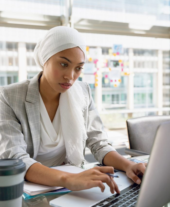 Front view of businesswoman in hijab working on laptop at desk in a modern office. Modern corporate start up new business concept with entrepreneur working hard